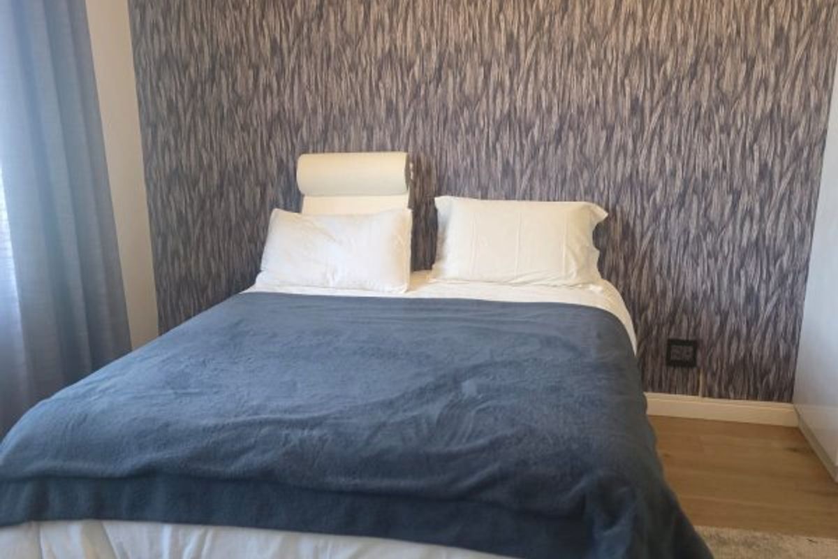 A well-maintained bedroom featuring textured feature wallpaper and laminate flooring.