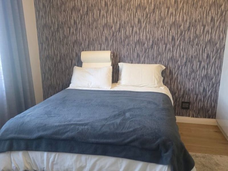A well-maintained bedroom featuring textured feature wallpaper and laminate flooring.
