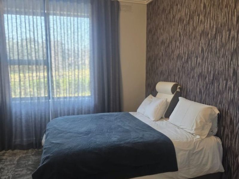 A well-maintained bedroom featuring textured accent wallpaper, coving, and timber flooring, providing a comfortable and neutral living space.