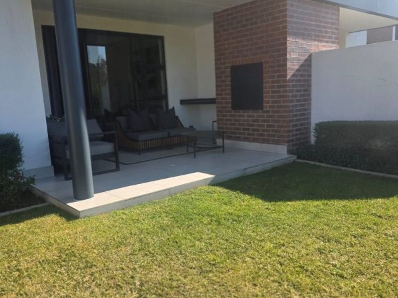 A covered ground-floor patio featuring a built-in fireplace, tiled flooring, and a brick feature wall, overlooking a private garden area.