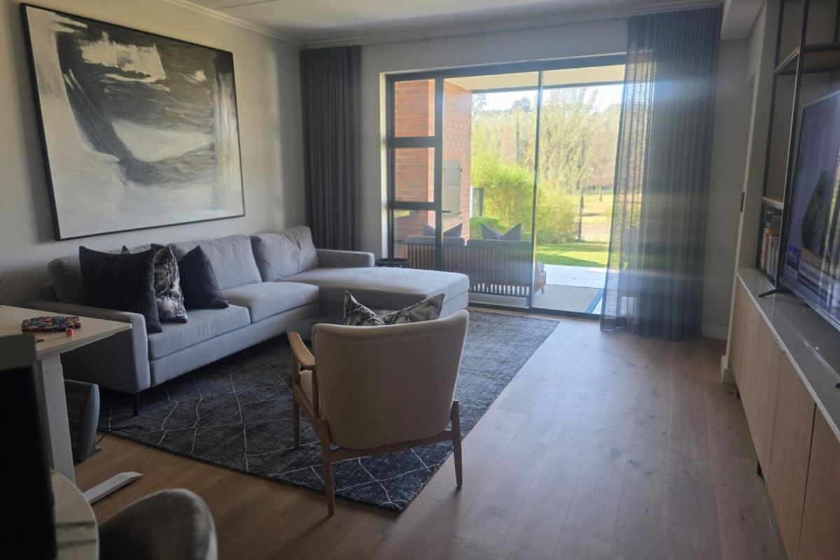 A well-lit living room featuring engineered wood flooring, built-in cabinetry, and large sliding glass doors that provide access to an outdoor patio area.