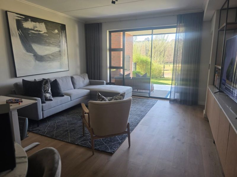 A well-lit living room featuring engineered wood flooring, built-in cabinetry, and large sliding glass doors that provide access to an outdoor patio area.