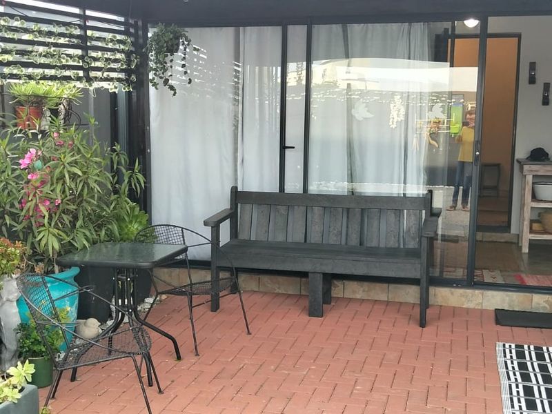 A covered outdoor patio area featuring brick paving, a black metal pergola structure, and sliding glass doors providing access to the interior living space.