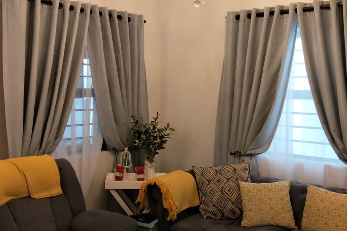 A cozy living room corner featuring dual windows with security bars and installed curtain rods, providing natural light and a comfortable atmosphere.