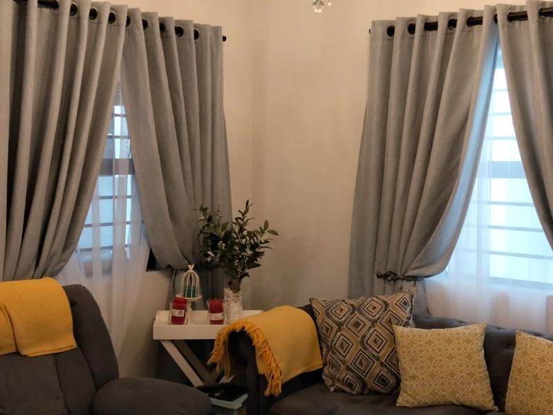 A cozy living room corner featuring dual windows with security bars and installed curtain rods, providing natural light and a comfortable atmosphere.