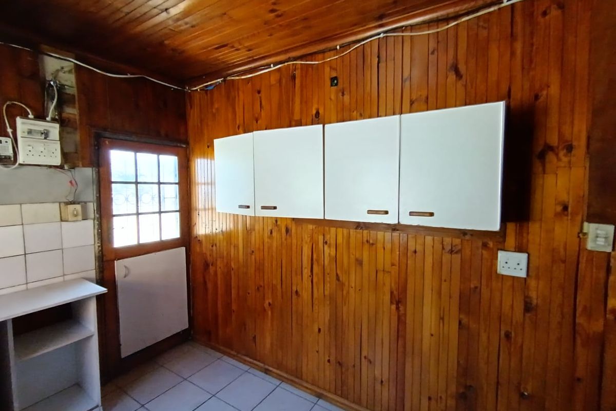 A functional kitchen area featuring timber wall and ceiling paneling, white wall-mounted cabinets, tiled flooring, and direct access to the exterior.