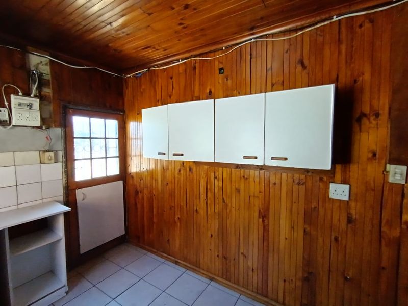 A functional kitchen area featuring timber wall and ceiling paneling, white wall-mounted cabinets, tiled flooring, and direct access to the exterior.