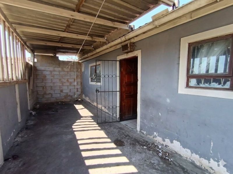 A covered outdoor patio area featuring a concrete floor, security gate, and exposed brickwork, requiring maintenance and cosmetic updates.