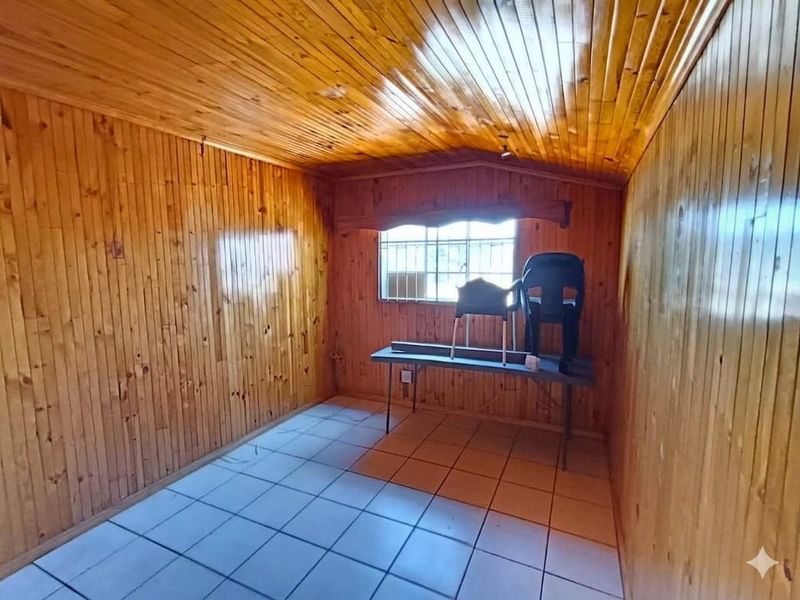 A bedroom featuring extensive timber wall and ceiling cladding with ceramic floor tiles and security bars on the window.
