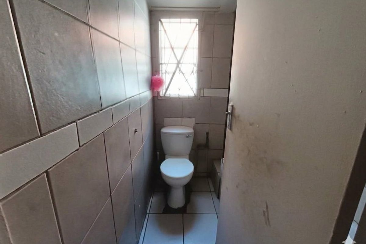 A compact, tiled bathroom featuring a standard toilet and a window with security bars, requiring cosmetic updates to improve its overall condition.