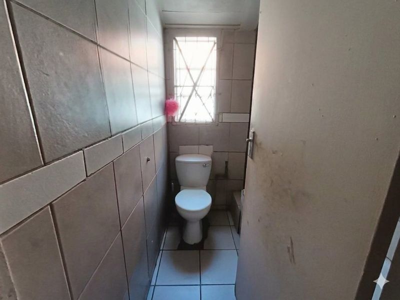 A compact, tiled bathroom featuring a standard toilet and a window with security bars, requiring cosmetic updates to improve its overall condition.
