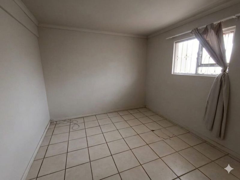 An empty bedroom featuring tiled flooring and a window with security bars, requiring some maintenance to the flooring.