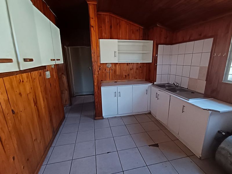 A dated kitchen featuring timber wall paneling, tiled flooring, and basic built-in cabinetry with a stainless steel sink.