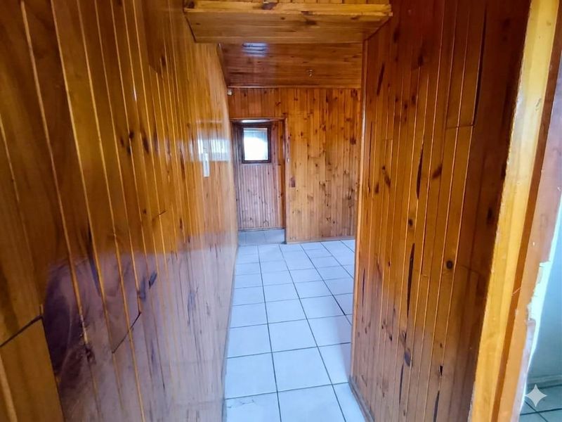 A narrow hallway featuring extensive timber wall and ceiling paneling with tiled flooring, presenting a dated aesthetic.