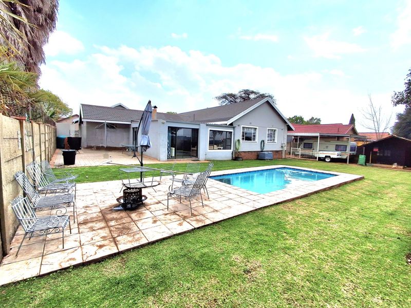 Rear exterior view of the property featuring a swimming pool, paved patio area, and a well-maintained garden space.
