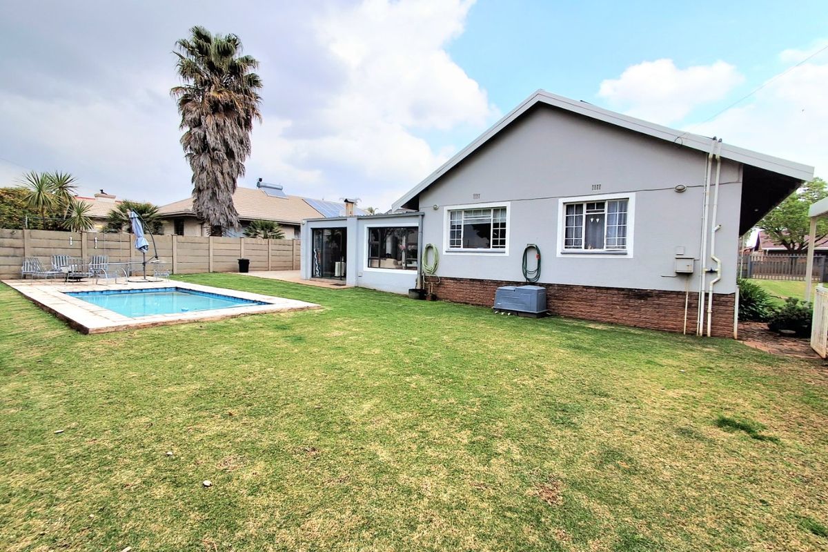 Rear view of the property featuring a swimming pool, a spacious lawn, and a brick and plaster exterior finish.