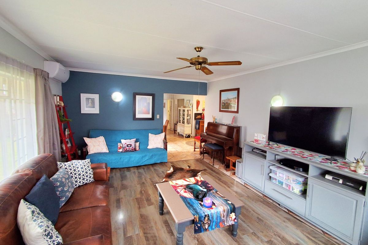 A comfortable living room featuring laminate flooring, a ceiling fan, wall-mounted air conditioning, and a feature wall with accent lighting.