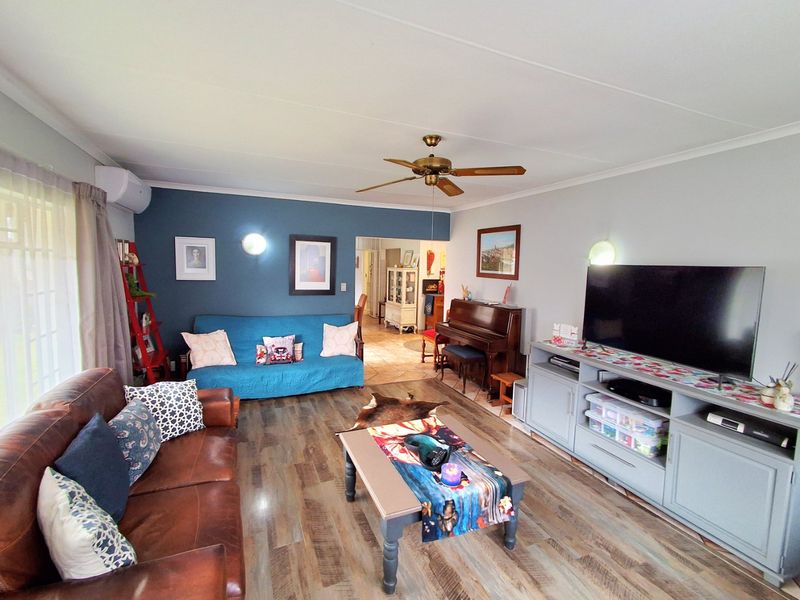 A comfortable living room featuring laminate flooring, a ceiling fan, wall-mounted air conditioning, and a feature wall with accent lighting.