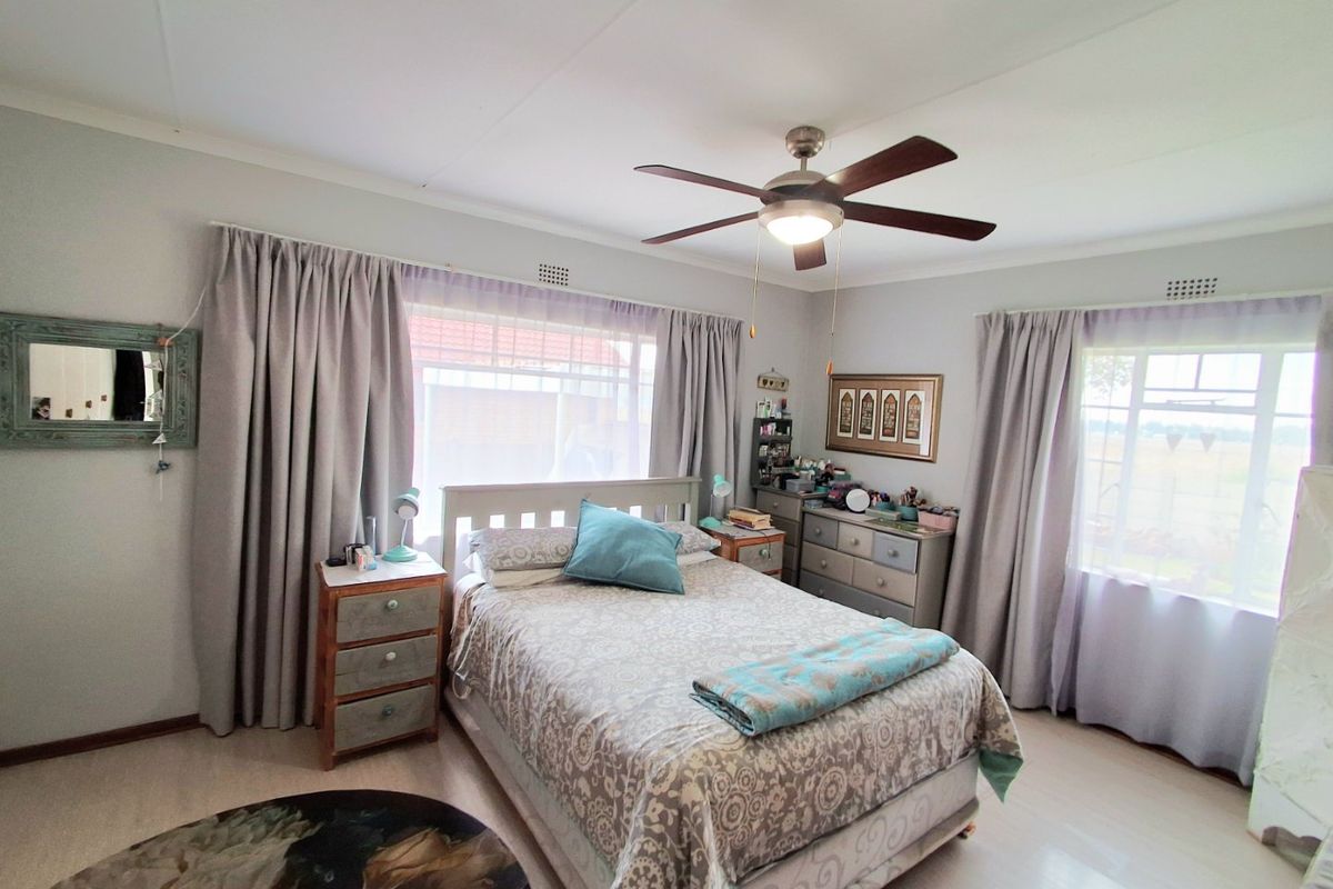 A well-lit bedroom featuring laminate flooring, a central ceiling fan, and large windows that provide ample natural light.