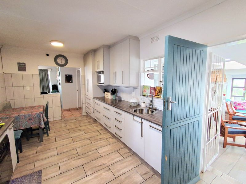 A functional kitchen featuring light-toned cabinetry, laminate countertops, a stainless steel sink, and tiled flooring, with a distinctive blue stable door.