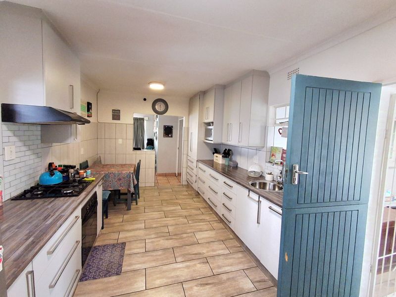 A functional kitchen featuring white cabinetry, laminate countertops, a gas hob with extractor, and tiled flooring, leading into an adjacent dining area.