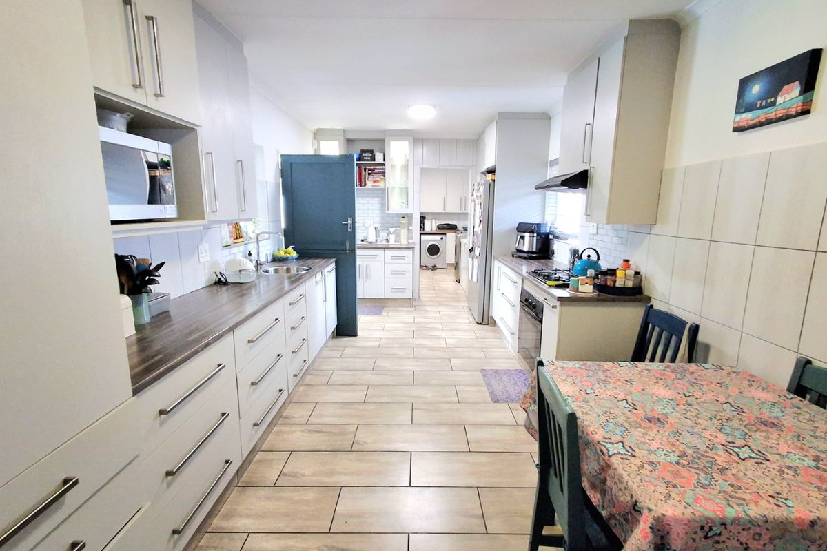 A functional kitchen featuring extensive built-in cabinetry, laminate countertops, a gas hob with extractor, and tiled flooring, with an integrated laundry area.