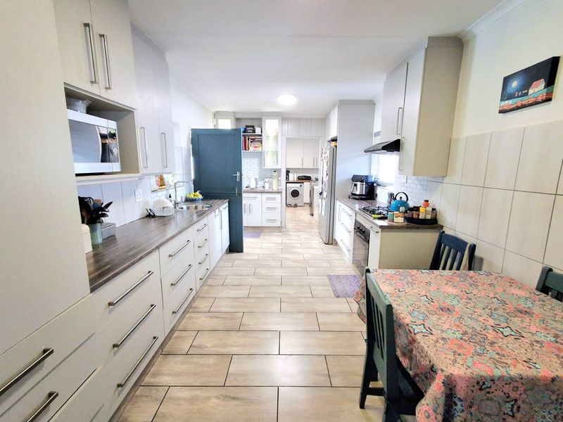 A functional kitchen featuring extensive built-in cabinetry, laminate countertops, a gas hob with extractor, and tiled flooring, with an integrated laundry area.