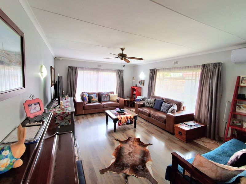 A spacious living room featuring laminate flooring, a ceiling fan, and wall-mounted air conditioning, offering a comfortable and functional living space.