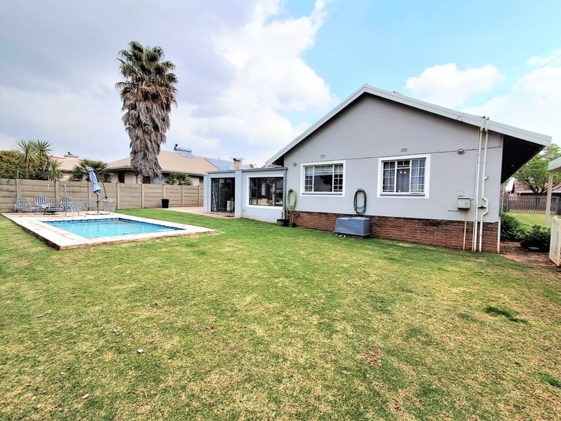 Rear view of the property featuring a swimming pool, a spacious lawn, and a brick and plaster exterior finish.
