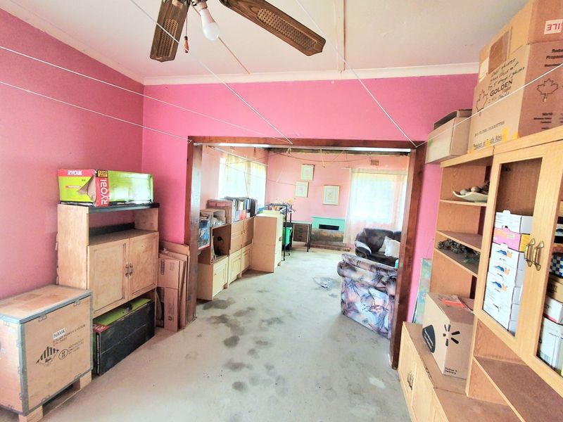 An open-plan living area featuring a ceiling fan and timber door frame, requiring cosmetic updates and flooring restoration to improve the space.