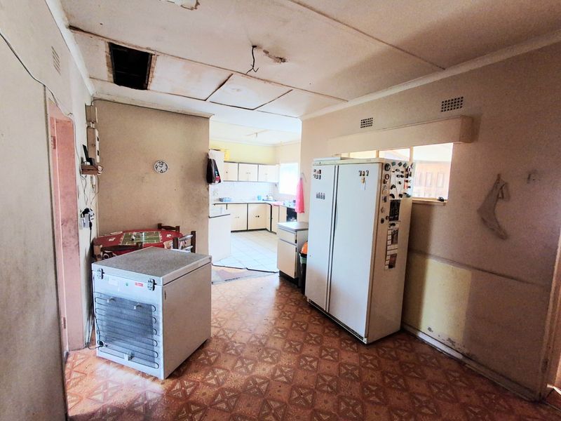 Open plan kitchen and dining area featuring dated cabinetry and flooring, requiring significant maintenance and cosmetic updates to restore functionality and aesthetic appeal.