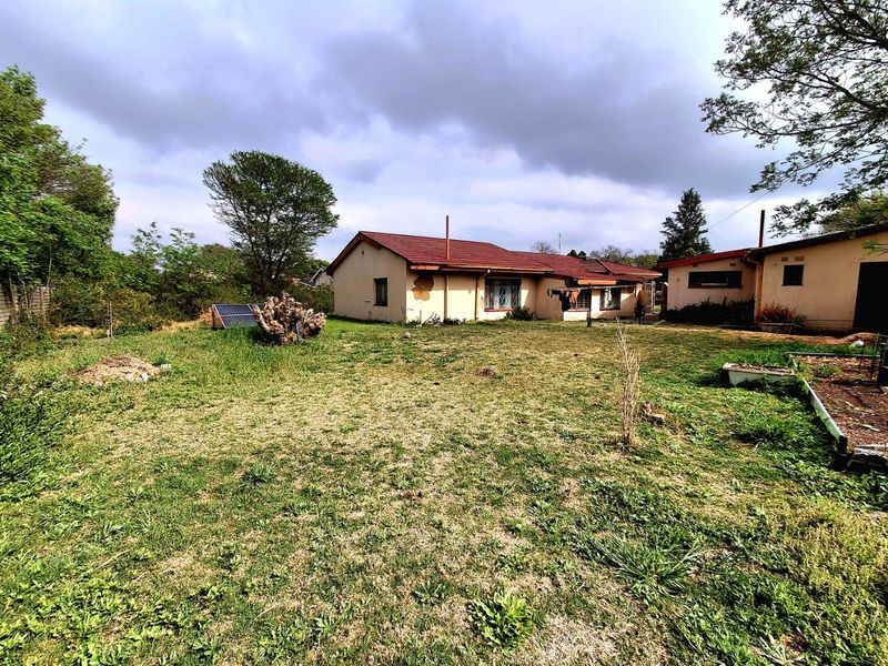 Rear view of the house featuring a large garden, tiled roof, and exterior wall finishes requiring maintenance.