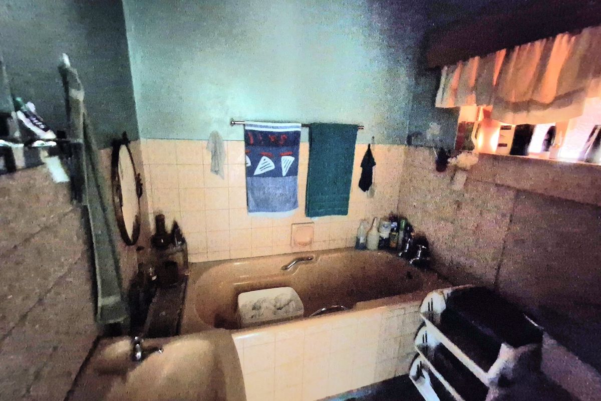 A dated bathroom featuring a built-in bathtub and wall-mounted basin with original tiled splashbacks, requiring modernization and cosmetic updates.