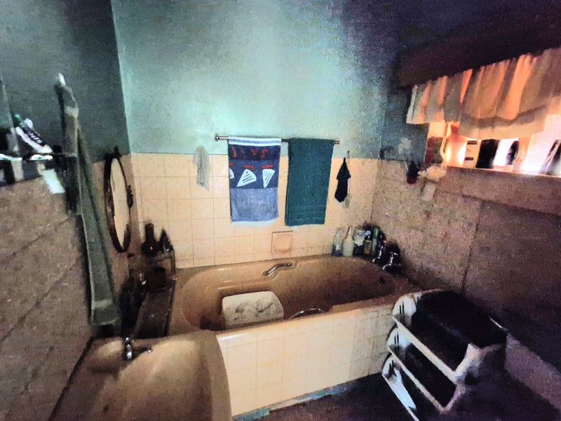 A dated bathroom featuring a built-in bathtub and wall-mounted basin with original tiled splashbacks, requiring modernization and cosmetic updates.