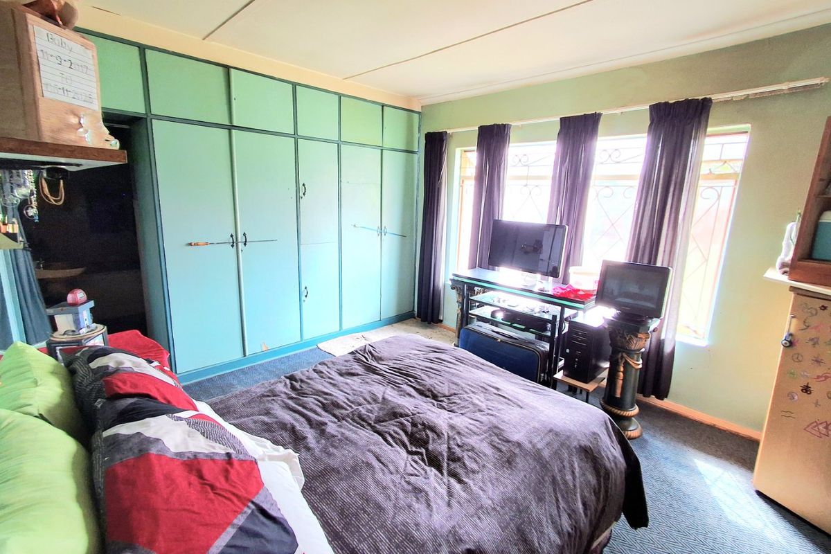 A bedroom featuring extensive built-in cupboards, security bars on the windows, and carpeted flooring, offering a functional space with potential for cosmetic updates.