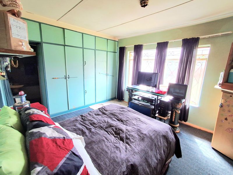 A bedroom featuring extensive built-in cupboards, security bars on the windows, and carpeted flooring, offering a functional space with potential for cosmetic updates.