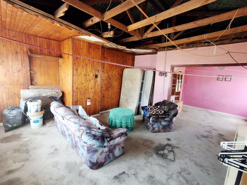 A living area featuring exposed timber roof trusses, timber wall paneling, and concrete flooring, currently requiring significant renovation and ceiling repairs.