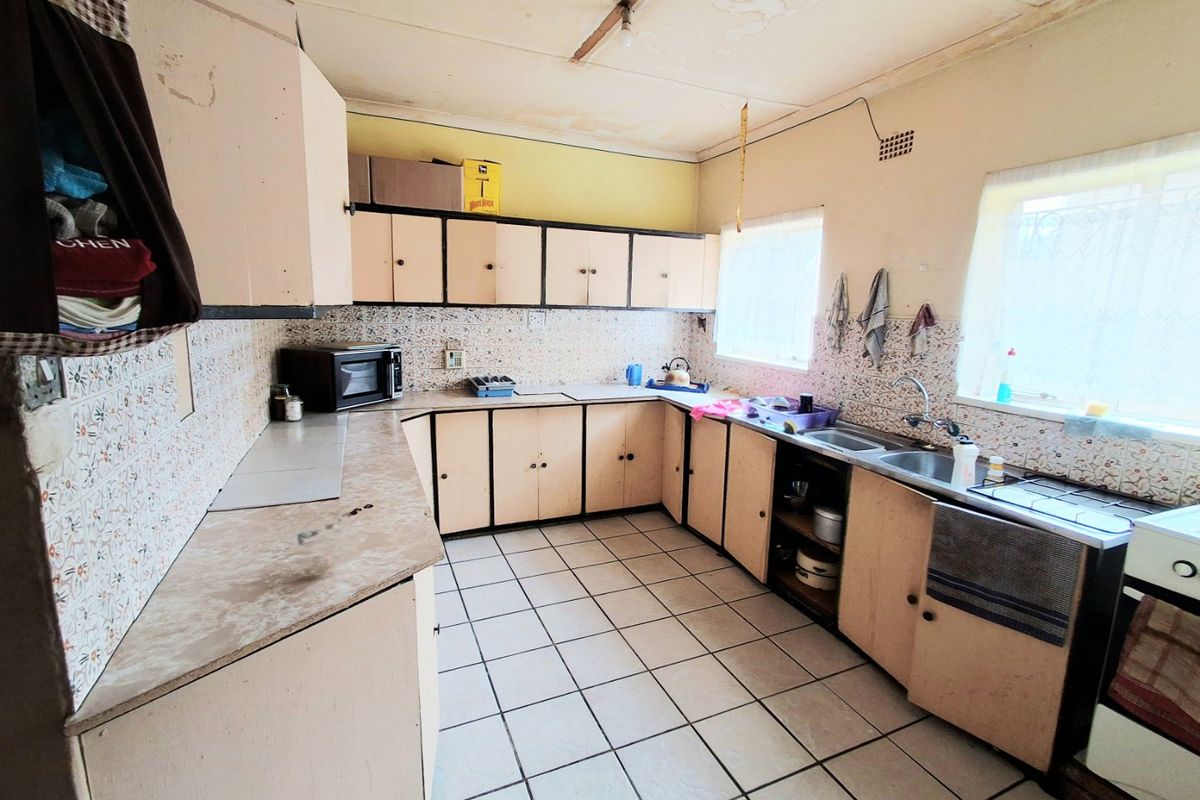 A dated kitchen featuring original laminate cabinetry, tiled backsplash, and ceramic flooring, requiring renovation to modernize the space.