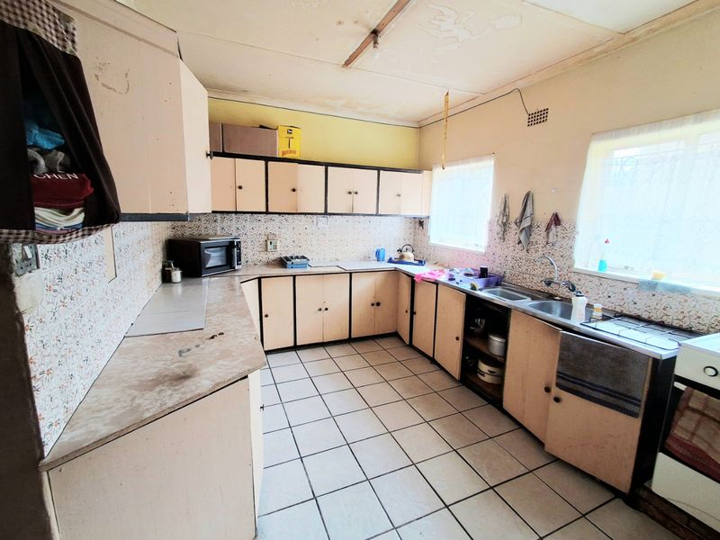 A dated kitchen featuring original laminate cabinetry, tiled backsplash, and ceramic flooring, requiring renovation to modernize the space.