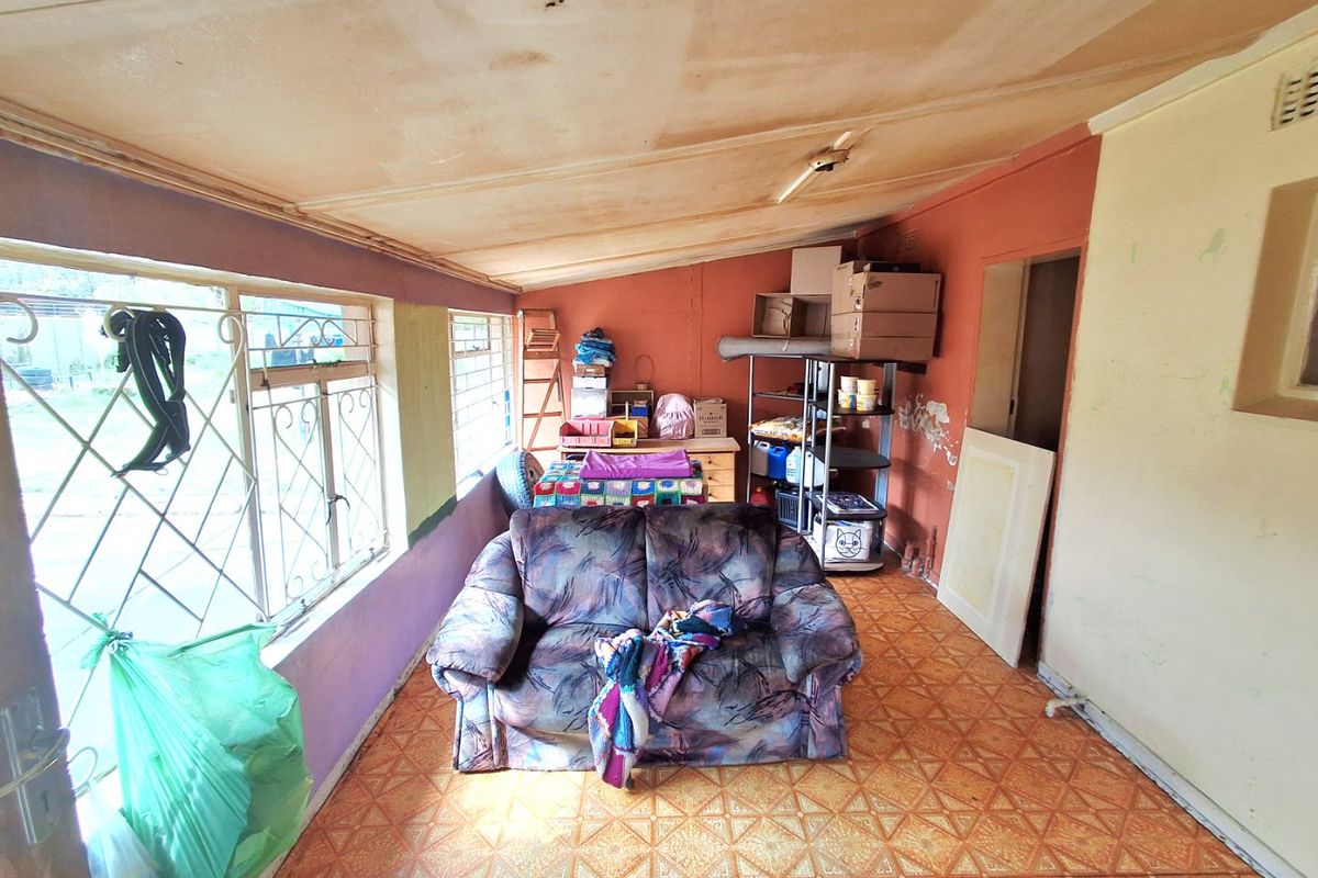 A living area featuring tiled flooring, security bars on windows, and a sloped ceiling, currently requiring cosmetic repairs and maintenance to the walls and ceiling.