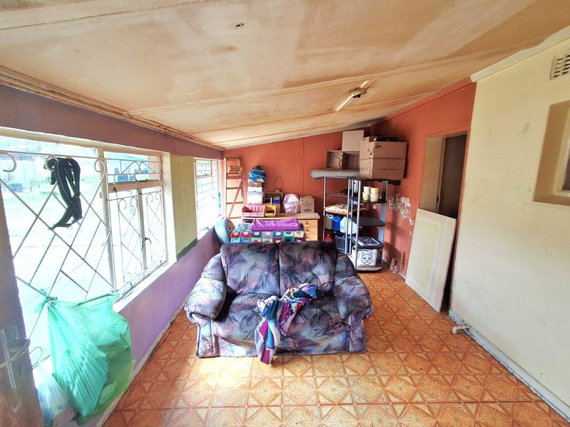A living area featuring tiled flooring, security bars on windows, and a sloped ceiling, currently requiring cosmetic repairs and maintenance to the walls and ceiling.