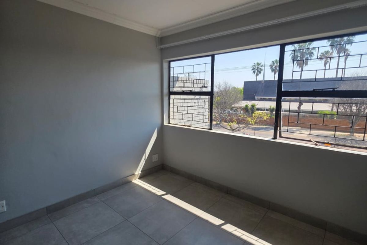 A bright, empty bedroom featuring neutral tiled flooring, coving, and large windows fitted with security bars, offering a clean and versatile living space.
