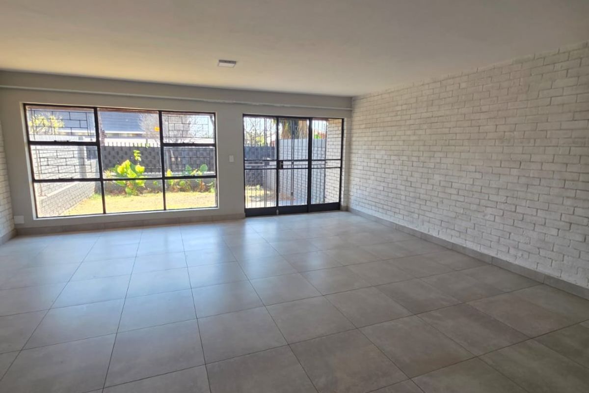 Spacious, light-filled living area featuring large format floor tiles, a painted brick feature wall, and direct access to the rear garden.