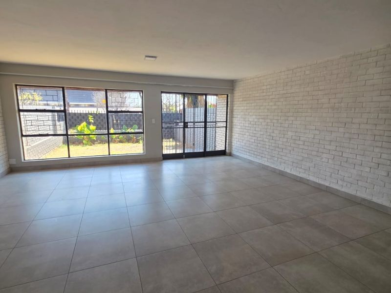 Spacious, light-filled living area featuring large format floor tiles, a painted brick feature wall, and direct access to the rear garden.