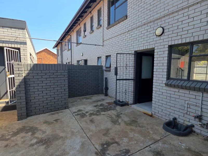 Rear exterior view of the townhouse featuring a concrete patio area, brick facade, security gate, and a functional utility sink.