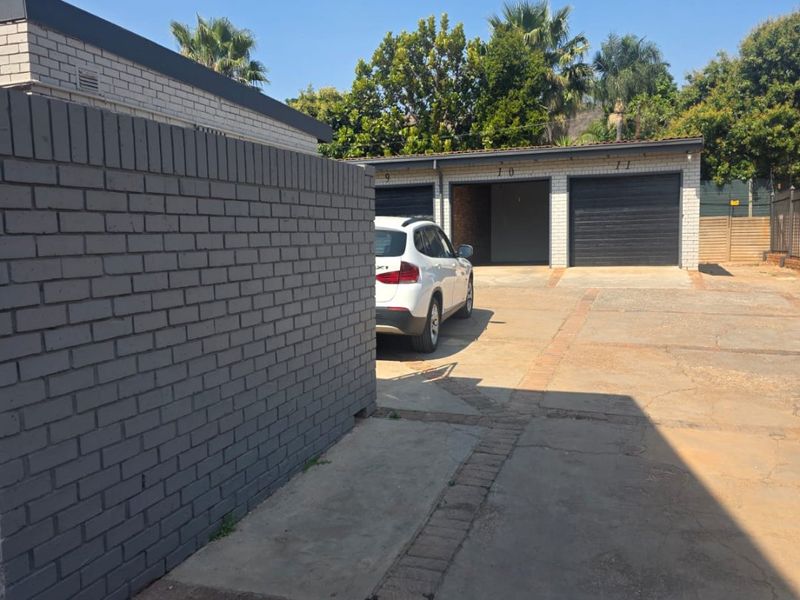 Exterior view of a townhouse complex featuring a shared concrete driveway, brick boundary wall, and multiple garage units.