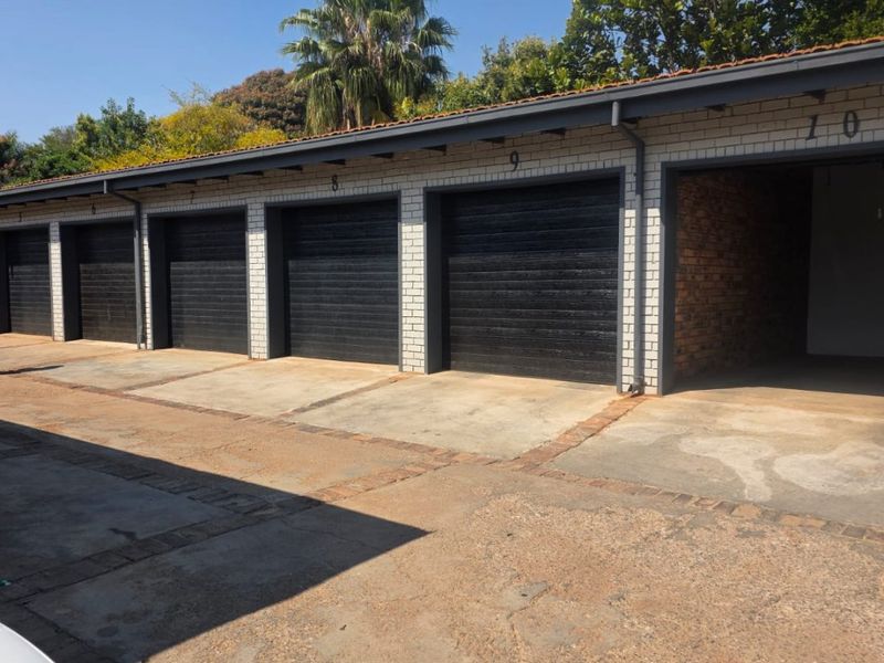 A row of multiple garage units featuring black roller doors, brick construction, and a shared concrete driveway area.