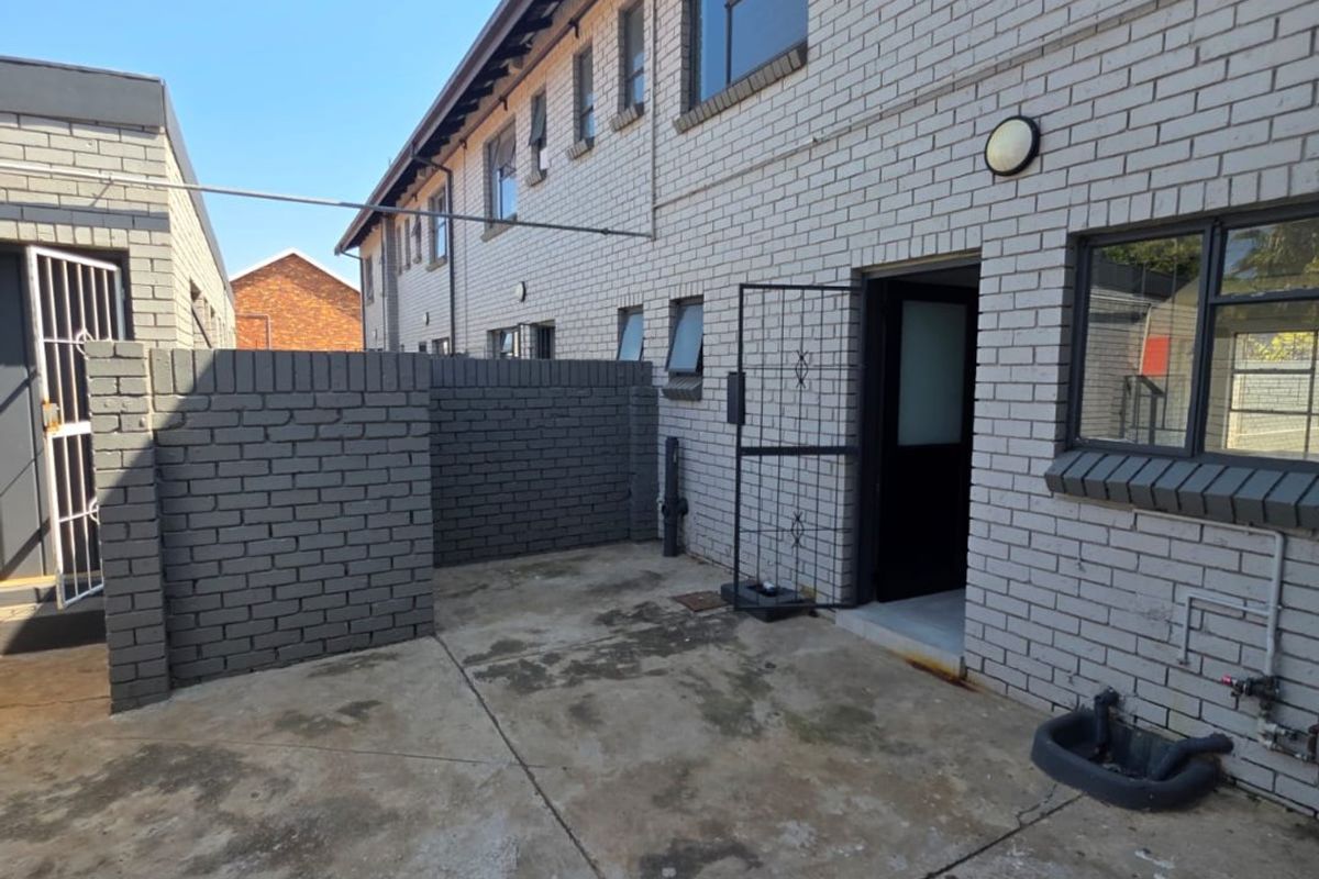 Rear exterior view of the townhouse featuring a concrete patio area, brick facade, security gate, and a functional utility sink.