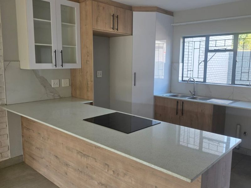 Modern kitchen featuring light wood-grain cabinetry, quartz countertops, a built-in induction hob, and a double basin sink with a window view.