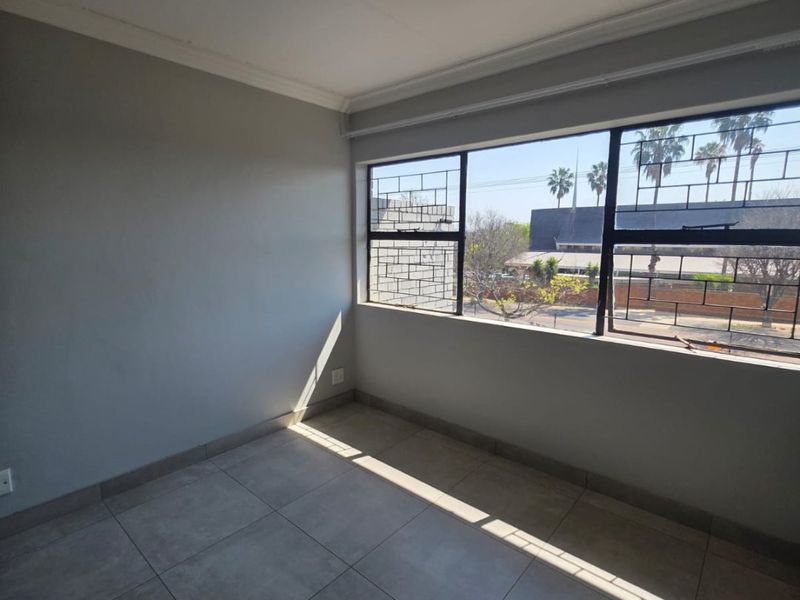 A bright, empty bedroom featuring neutral tiled flooring, coving, and large windows fitted with security bars, offering a clean and versatile living space.
